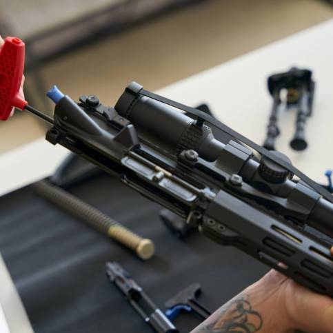 Tool for cleaning firearms in male hands Man cleans a disassembled firearm with a special tool on a napkin, parts of the machine gun are laid out